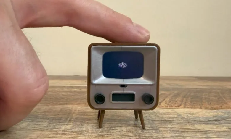 Miniature retro TV with a sparkling object on the screen, dwarfed by a person's finger.