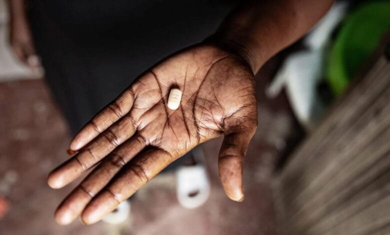 Close-up of a dark hand gently holding a single light beige pill.
