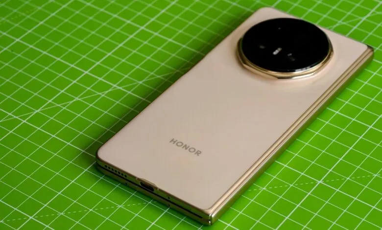 Gold Honor Magic V5 phone on green surface, showcasing its circular camera design.