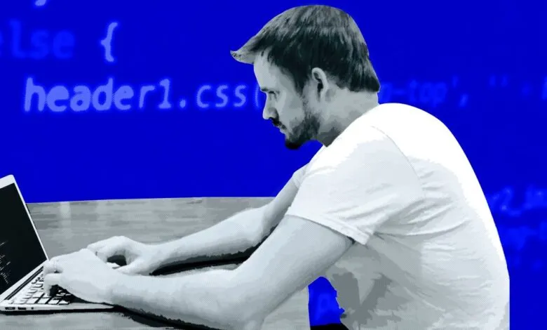 Man focused on coding, typing on laptop with code visible on screen and in background.