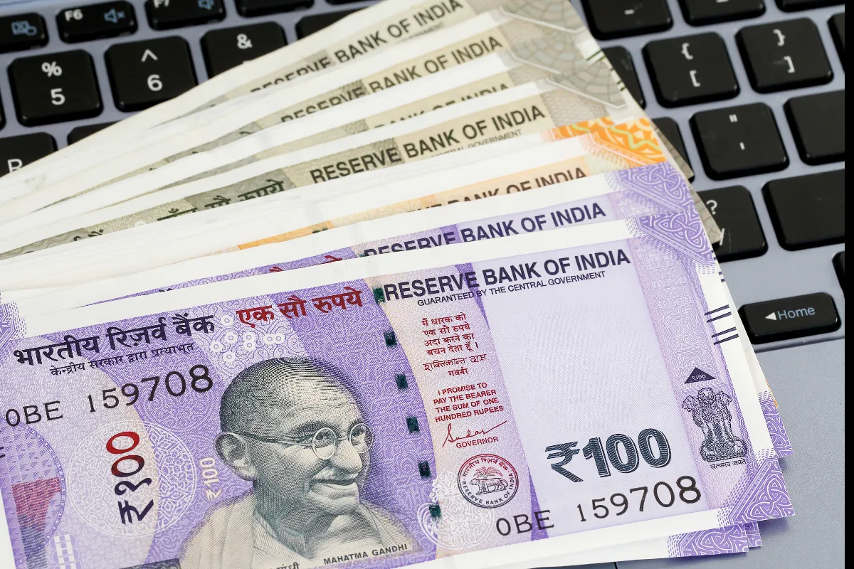 Indian 100 rupee notes on a laptop keyboard, illustrating online banking or digital transactions.