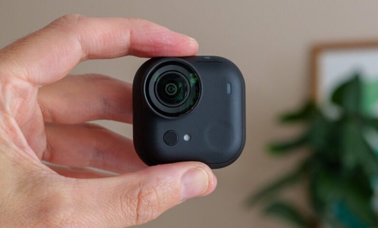 A hand holds a small, black Insta360 Go 2 action camera. The camera's lens is prominent.
