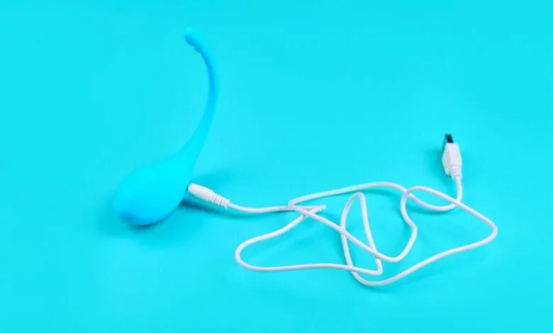 A vibrant blue sex toy with a curved design is shown connected to a white USB charging cable against a bright turquoise background.