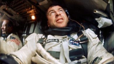 Close-up of astronaut James Lovell aboard Apollo 8, wearing a spacesuit and headset, inside a spacecraft.