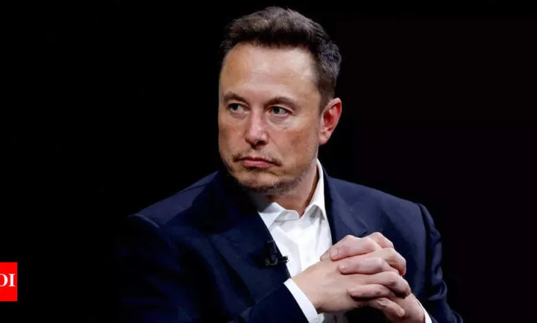 Elon Musk, CEO of Tesla and SpaceX, in a pensive pose, wearing a dark suit against a black background.
