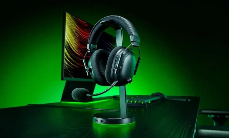 Razer BlackShark V3 Pro gaming headset on a stand, next to a computer monitor and keyboard, all illuminated in green.