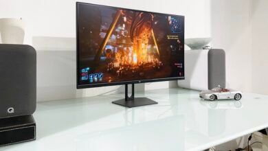 PC gaming setup with monitor displaying a video game scene, speakers, and a model car.