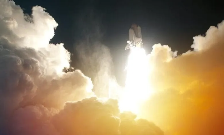 Space shuttle launching through bright clouds, fiery exhaust trail visible.