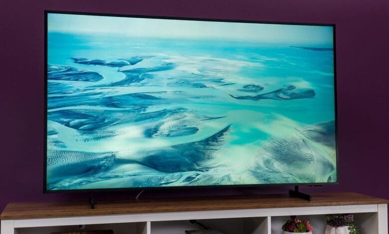 A large flat-screen TV displays an aerial shot of turquoise water flowing through sandy land.