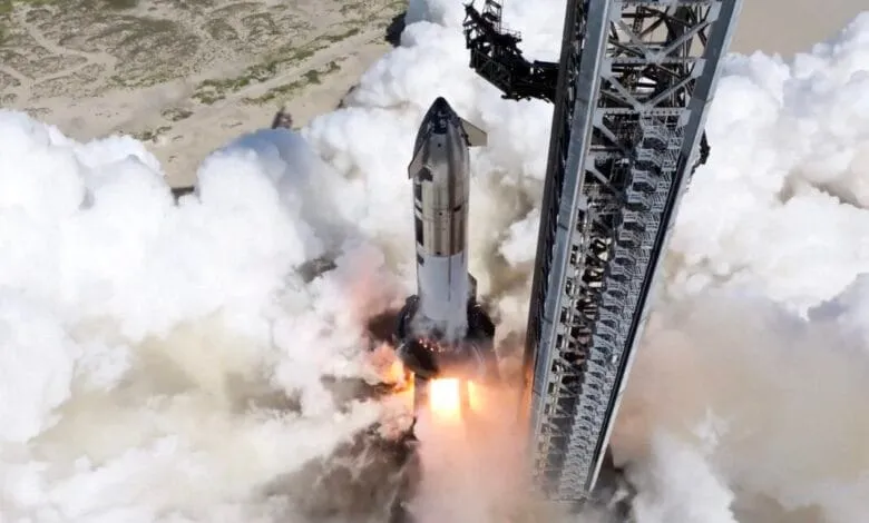 A rocket launches, surrounded by thick white smoke, from a tall metal launch tower.