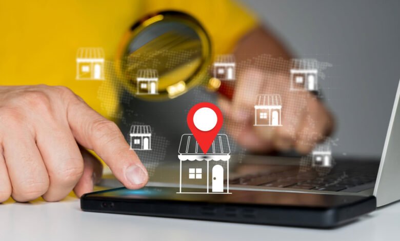 Person using phone and laptop to locate businesses on a map, using a magnifying glass to zoom in on a location.