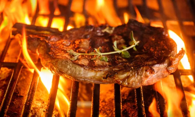 A juicy steak, seasoned with thyme, sizzles on a fiery grill.