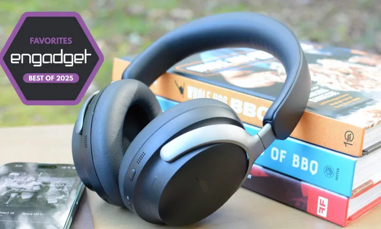 Engadget's Best of 2025: Black and silver headphones rest on books, near a phone playing music.
