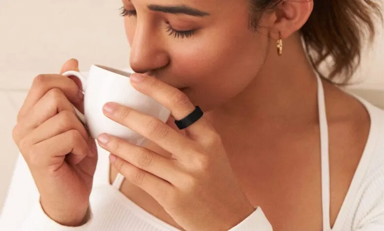 Close-up of a woman's hands holding a white cup, wearing a black ring; soft, warm lighting.