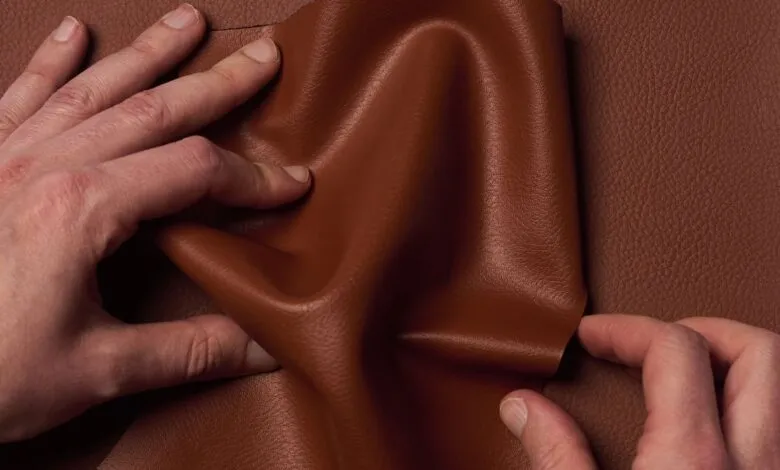 Hands gently hold and display a rich, brown leather sample, showcasing its texture and drape.