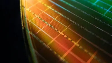 Close-up of a microchip's intricate circuitry, showcasing a grid pattern in warm orange and cool green hues.