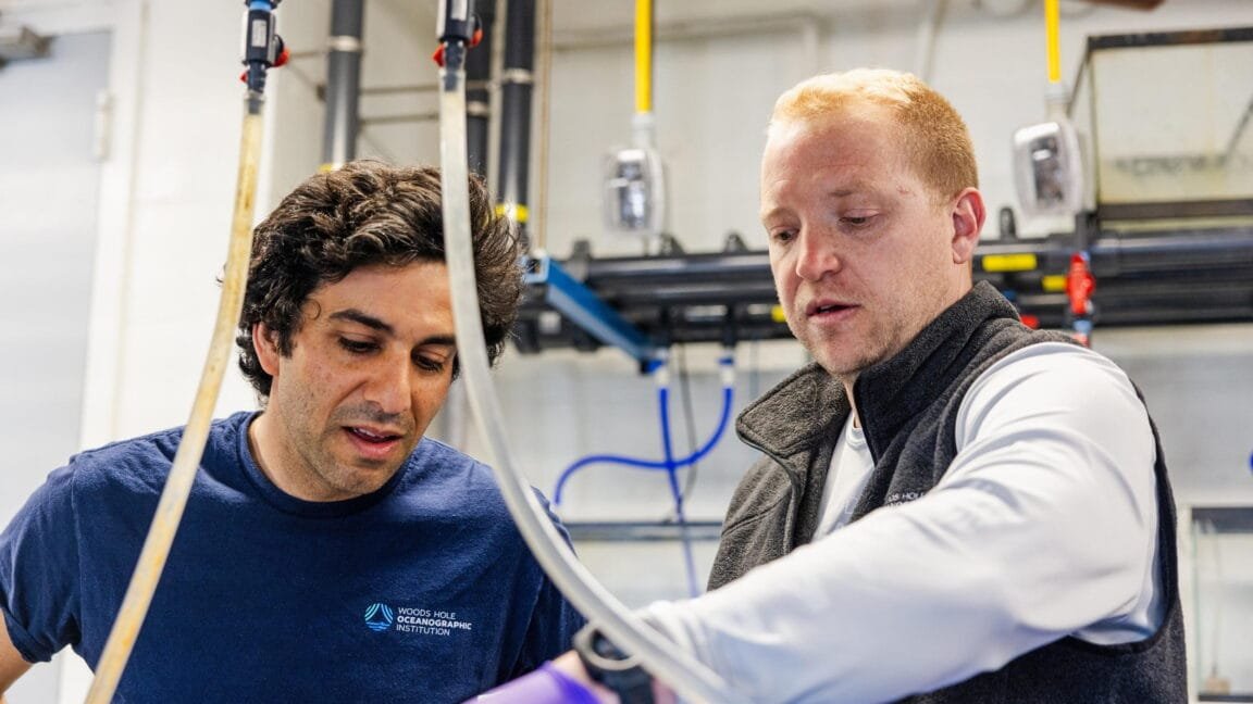Two scientists collaborate on equipment in a lab, examining tubing and apparatus.