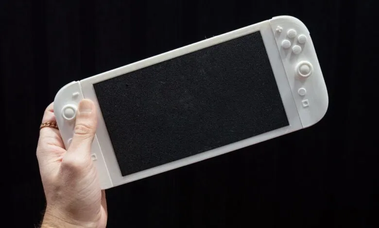 White 3D-printed Nintendo Switch mockup held in a hand against a black background.
