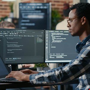 Focused programmer working on code on dual monitors in a busy office.