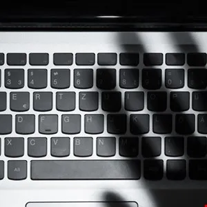 Close-up of a laptop keyboard with a shadowy hand-like shape cast upon it, suggesting online security or privacy concerns.