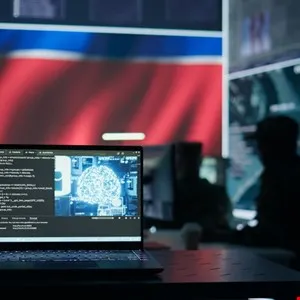 Laptop displaying brain-shaped code on screen, with blurred figures working in a cybersecurity command center in the background.