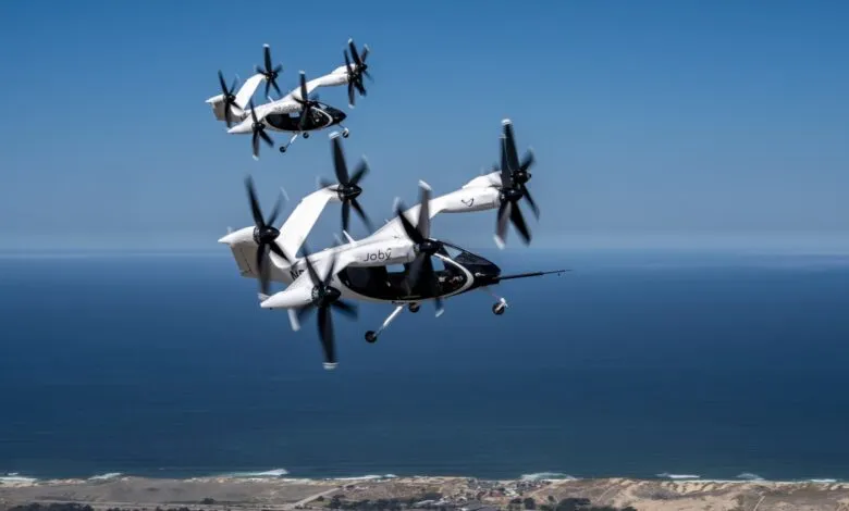 Two Joby Aviation electric vertical takeoff and landing (eVTOL) aircraft flying over a coastline.