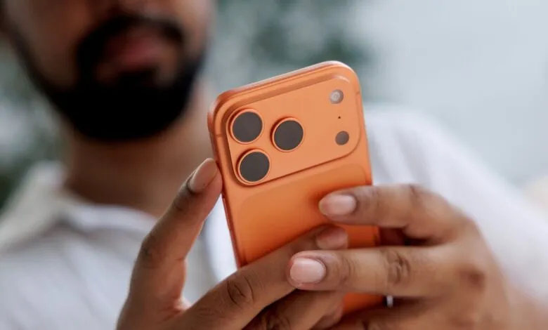 Close-up of a person holding an orange smartphone, focusing on the camera array.