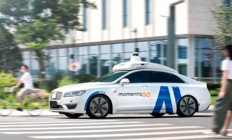 Self-driving car from MomentaGO navigating a city street, safely passing pedestrians and a cyclist.