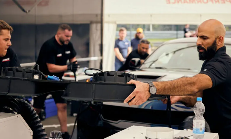 Mechanics working on a car, holding a large black component.