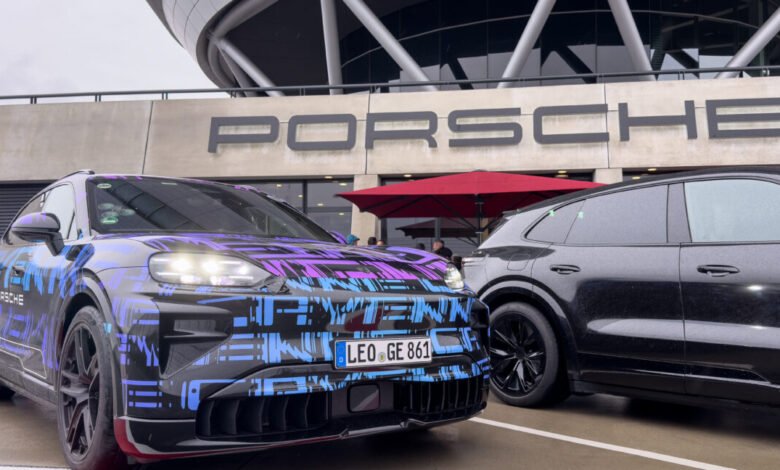 A camouflaged Porsche Cayenne prototype with a colorful wrap and a black Cayenne parked outside the Porsche building.