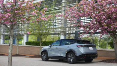 Sleek gray Nissan Ariya EV parked near pink cherry blossoms in front of a modern building.