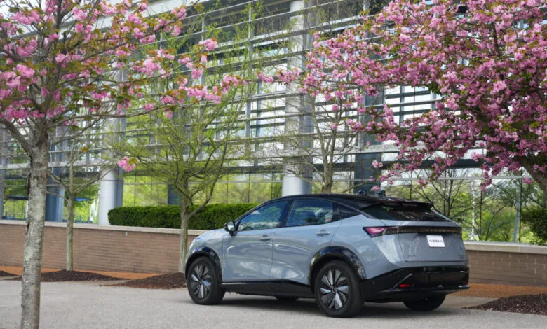 Sleek gray Nissan Ariya EV parked near pink cherry blossoms in front of a modern building.