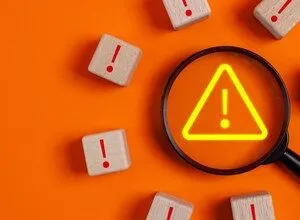 Magnifying glass over warning sign surrounded by exclamation point blocks.
