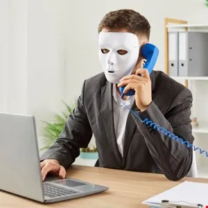 Businessman wearing a white mask talks on a vintage blue phone while working on a laptop.