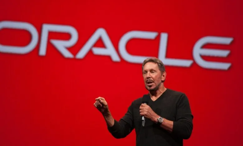 Larry Ellison speaks on stage in front of a large red Oracle logo.