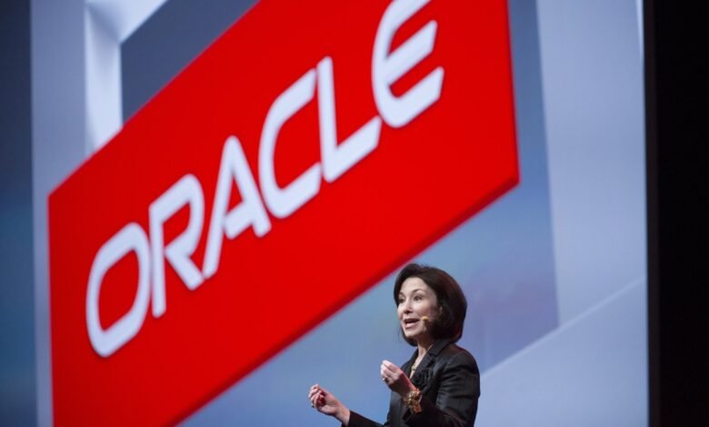 Safra Catz, Oracle CEO, speaks at a conference with the large red Oracle logo in the background.