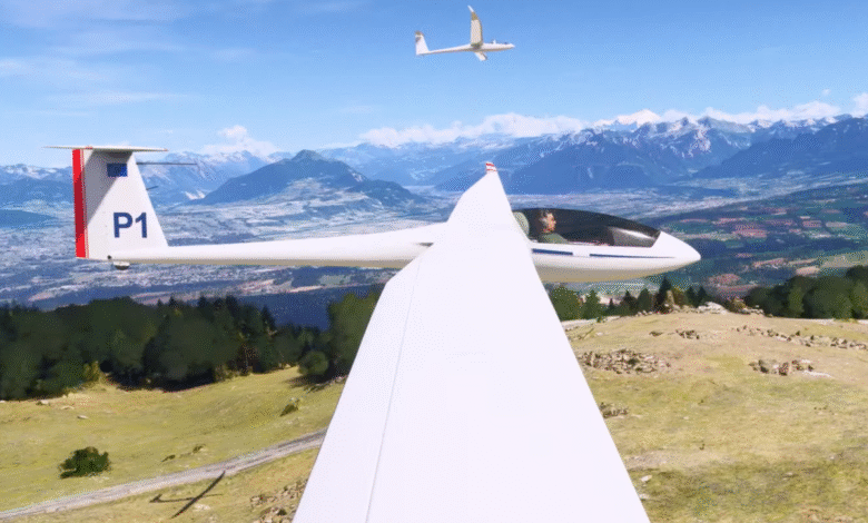 Pilot in a white glider flying over a green valley and mountains, with another glider in the sky.