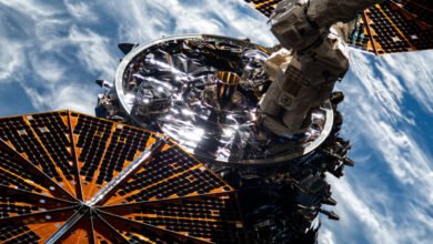 Close-up of a space station's exterior, showing solar panels, metallic components, and a robotic arm against a backdrop of Earth's atmosphere.