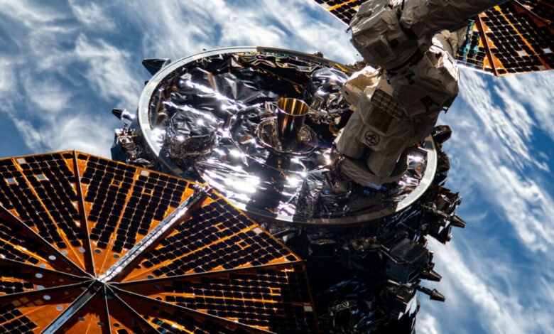 Close-up of a space station's exterior, showing solar panels, metallic components, and a robotic arm against a backdrop of Earth's atmosphere.