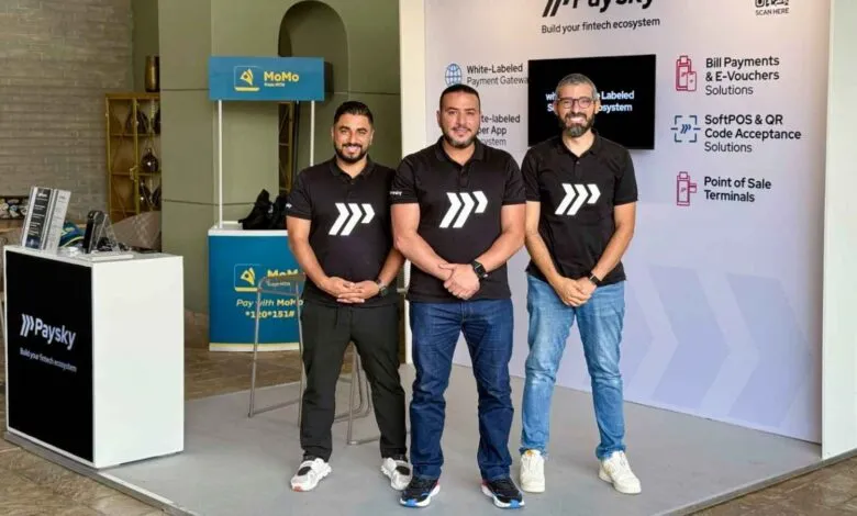 Three men in black Paysky t-shirts stand at a fintech booth, showcasing payment solutions.