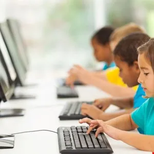 Diverse group of preschool children learning to type on computers in a classroom.