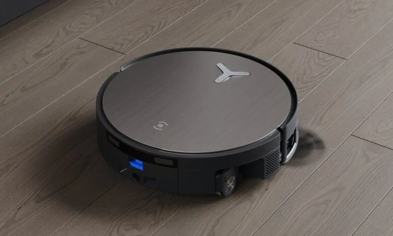 Smart robot vacuum cleaner on hardwood floor, dark gray metallic top, black base.