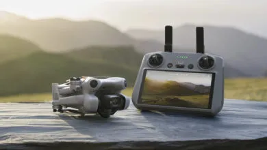 White drone and controller on a stone surface with a mountain landscape on the screen.