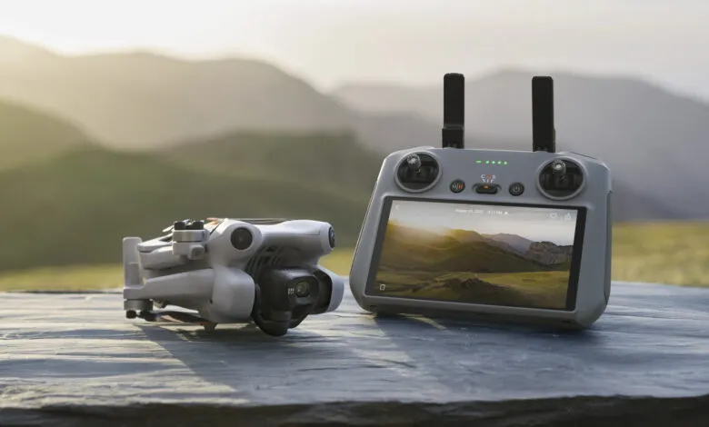 White drone and controller on a stone surface with a mountain landscape on the screen.