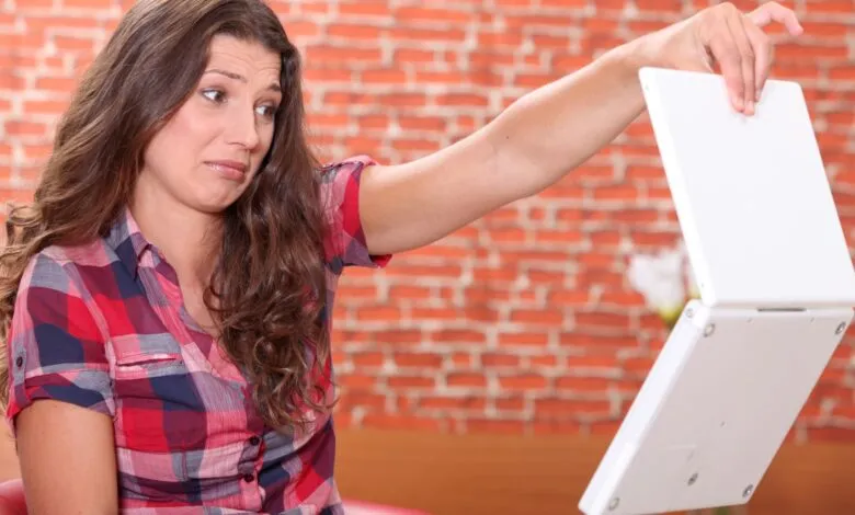 Woman with a frustrated expression holding a white laptop upside down.