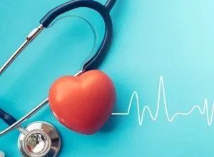 Red heart model next to a stethoscope and a heartbeat line on a blue background.