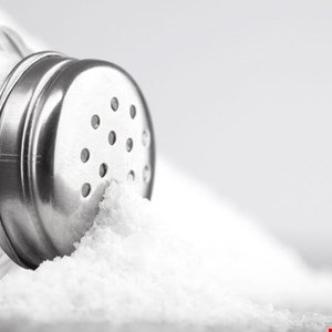 Close-up of salt spilling from a metal salt shaker onto a white surface.