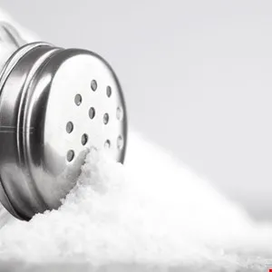 Close-up of salt spilling from a metal salt shaker onto a white surface.