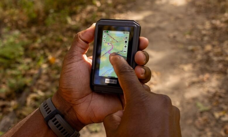 Person's hands holding a Garmin GPS device displaying a trail map outdoors.