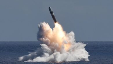 A Trident II D5 missile launches from the ocean, creating a massive plume of water and smoke.